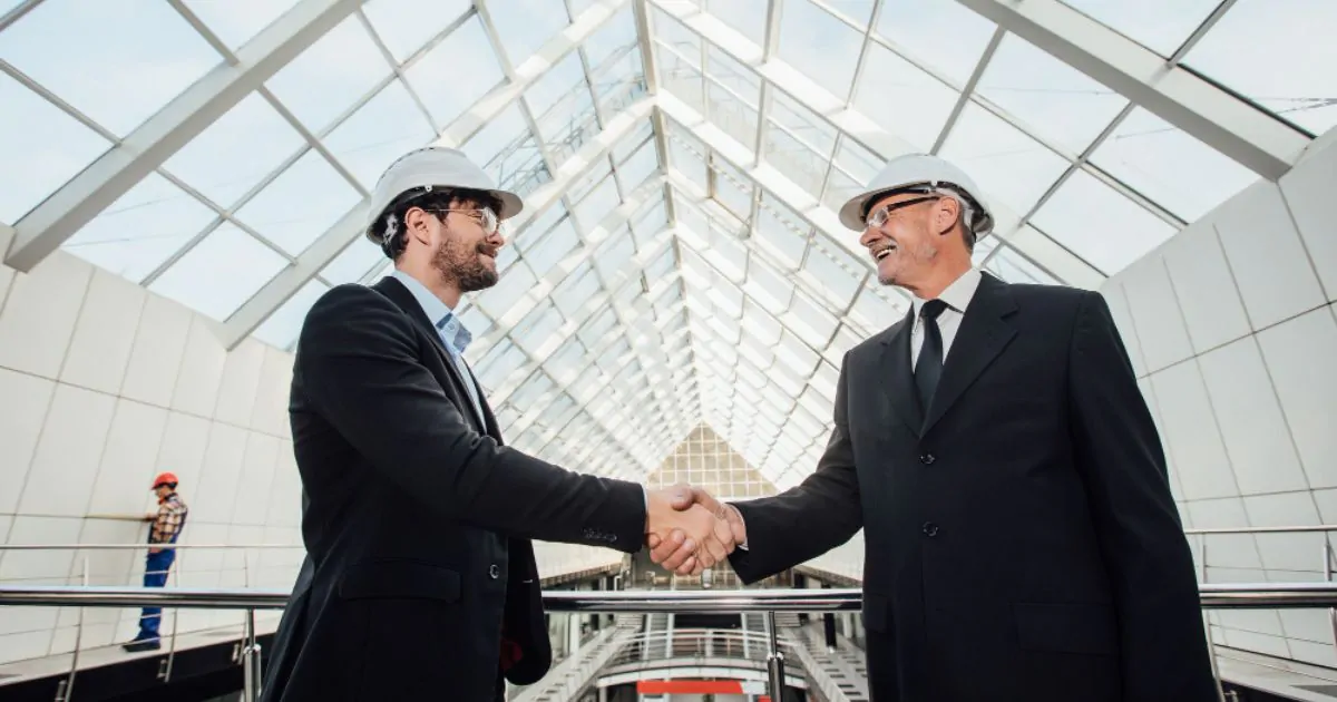 Two professionals shake hands outside glass building, signifying partnership in MEP Engineering.